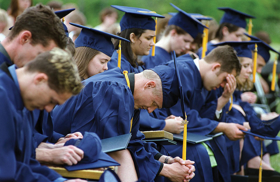 Students in blue cap and gowns with heads bowed